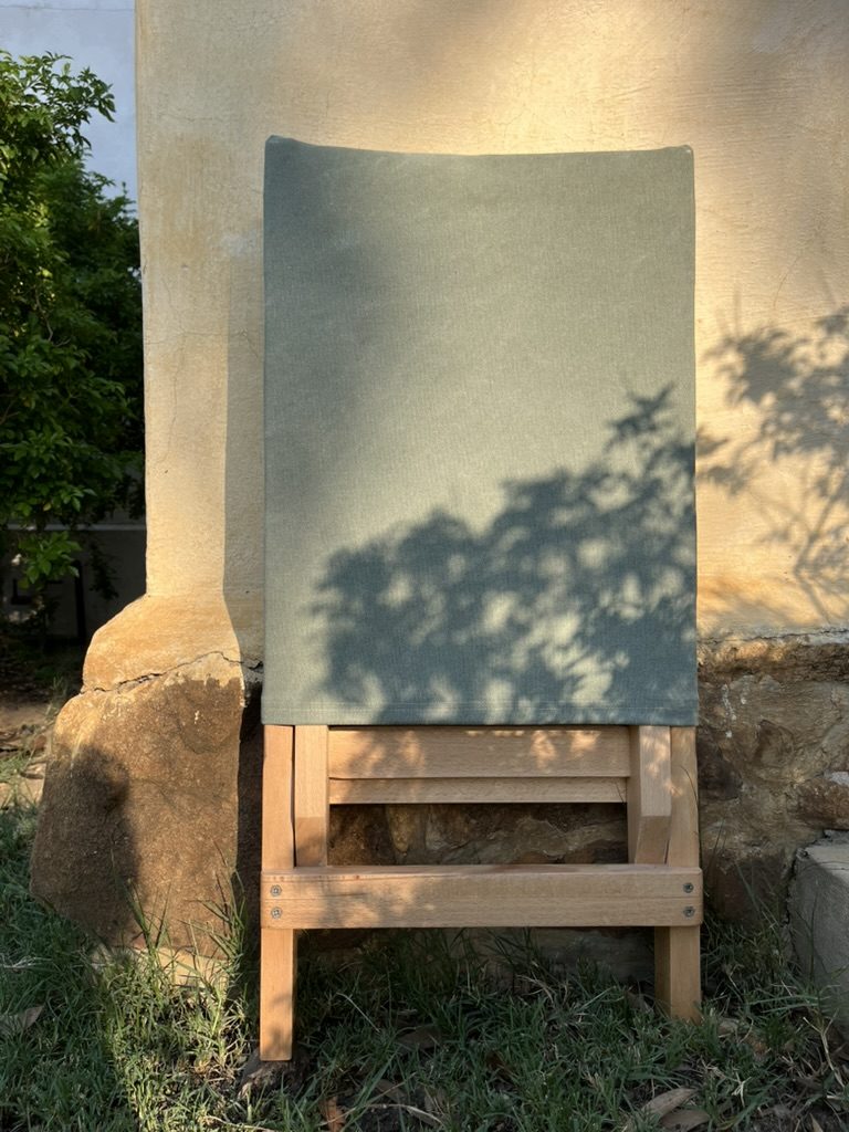Beech wood folding chair with olive canvas against a sunlit wall